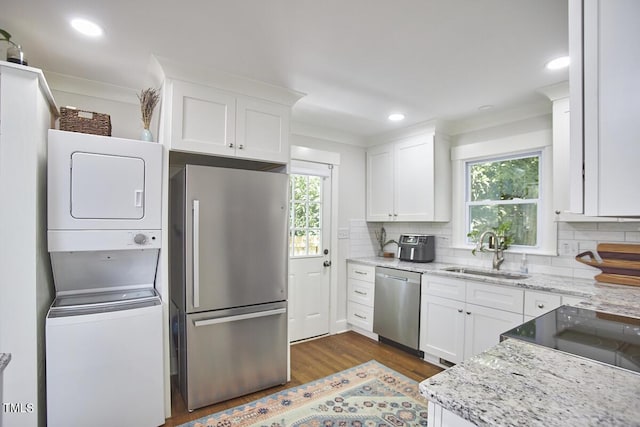 kitchen featuring appliances with stainless steel finishes, a sink, estacked washer and dryer, dark wood finished floors, and tasteful backsplash