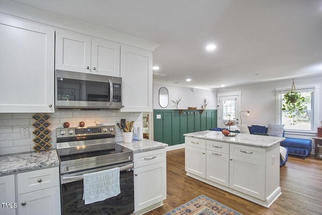 kitchen with appliances with stainless steel finishes, white cabinets, a kitchen island, dark wood-style flooring, and decorative backsplash
