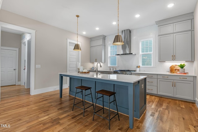 1029 Whitehall Cir, Durham, NC 27713 - kitchen featuring wall chimney range hood, gray cabinetry, a breakfast bar, a center island with sink, and light countertops
