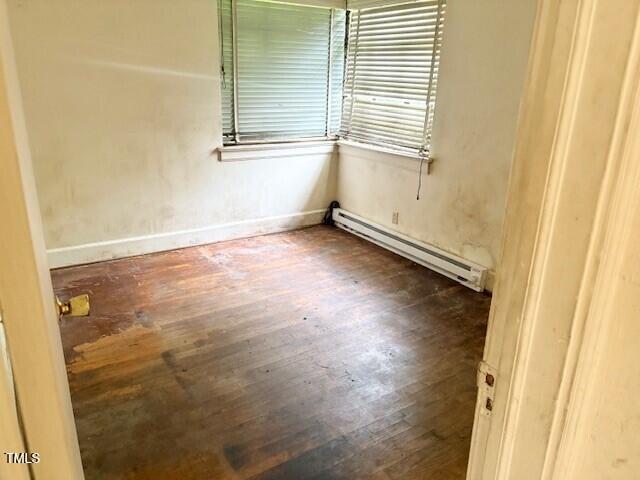 empty room with baseboard heating, wood finished floors, and baseboards