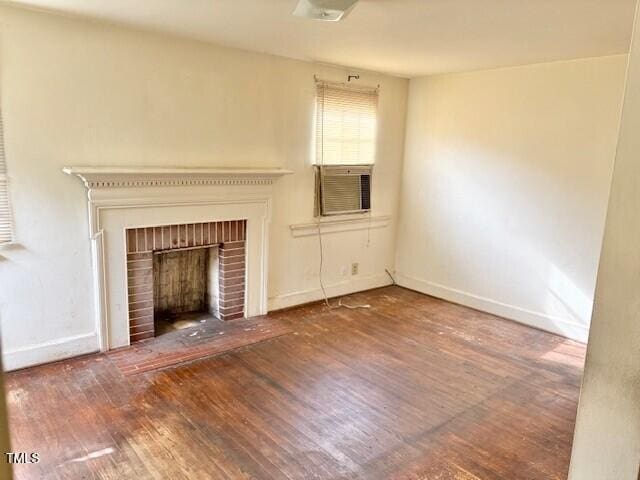 unfurnished living room with wood finished floors, cooling unit, a brick fireplace, and baseboards