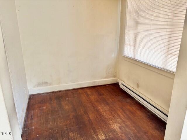 empty room featuring baseboard heating, dark wood finished floors, and baseboards
