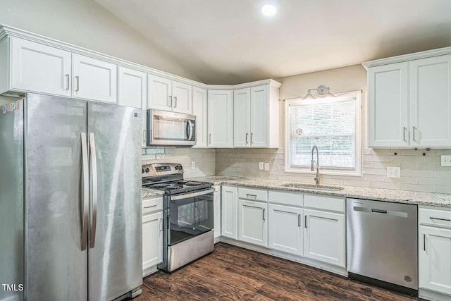 kitchen with appliances with stainless steel finishes, a sink, backsplash, white cabinets, and vaulted ceiling
