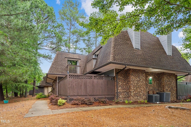 back of property with a shingled roof, a balcony, a chimney, brick siding, and mansard roof