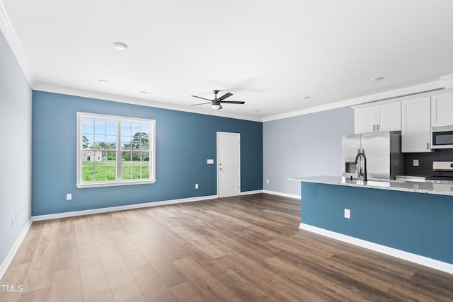 unfurnished living room with ornamental molding, a ceiling fan, dark wood finished floors, baseboards, and a sink