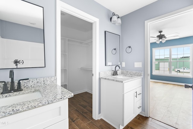full bathroom featuring two vanities, wood finished floors, ceiling fan, and baseboards