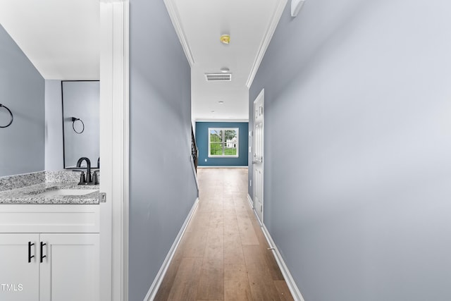 hall featuring a sink, light wood finished floors, baseboards, and ornamental molding