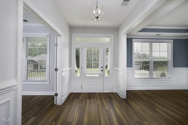 foyer entrance featuring a chandelier, dark wood finished floors, wainscoting, a decorative wall, and crown molding