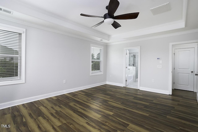 unfurnished bedroom with a tray ceiling, dark wood-type flooring, crown molding, baseboards, and ensuite bathroom