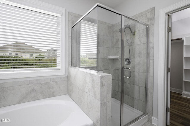 bathroom featuring a shower stall, a spacious closet, a garden tub, and wood finished floors