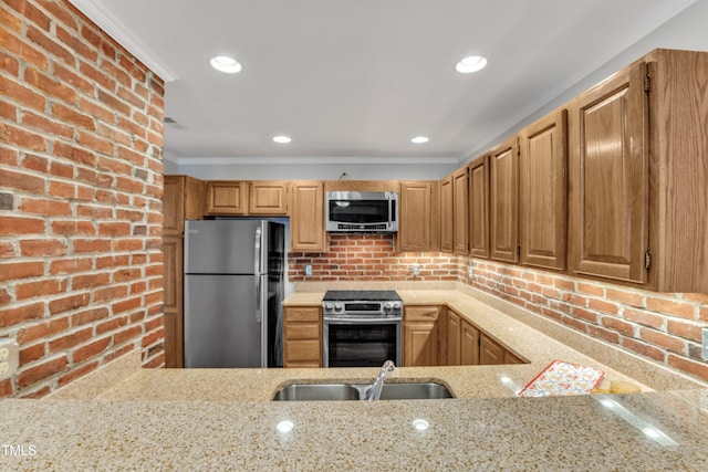 kitchen featuring appliances with stainless steel finishes, a sink, brick wall, light stone countertops, and crown molding