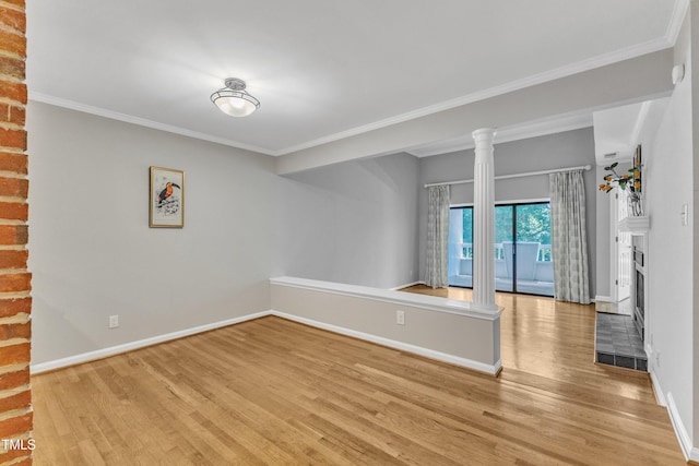 empty room with light wood finished floors, baseboards, decorative columns, ornamental molding, and a fireplace