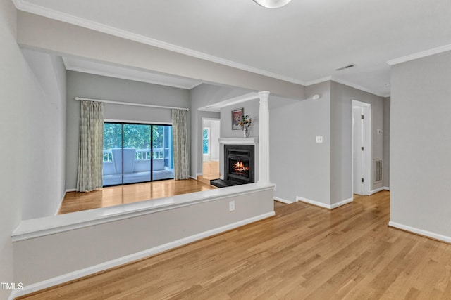 unfurnished living room featuring baseboards, wood finished floors, a warm lit fireplace, crown molding, and ornate columns