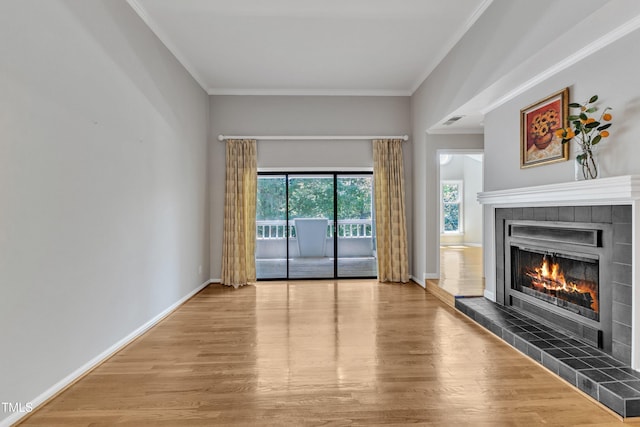 unfurnished living room with a tile fireplace, wood finished floors, crown molding, and baseboards