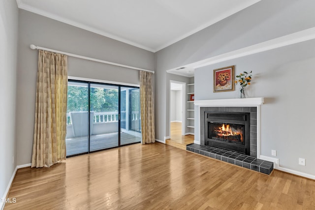 unfurnished living room featuring crown molding, a tiled fireplace, baseboards, and wood finished floors