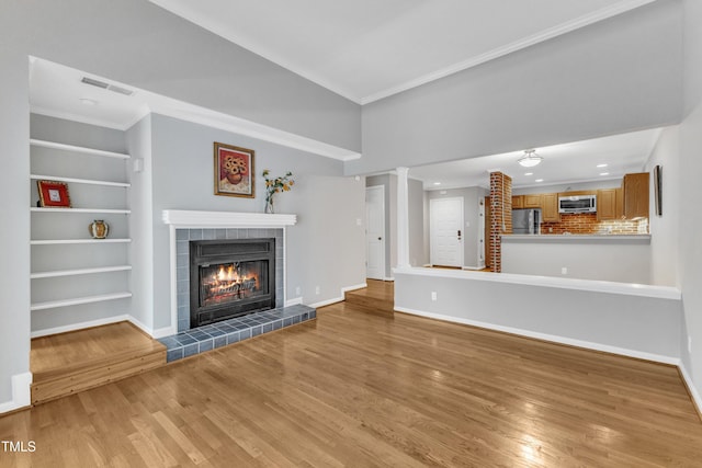 unfurnished living room featuring light wood-style flooring, a fireplace, baseboards, ornamental molding, and built in features