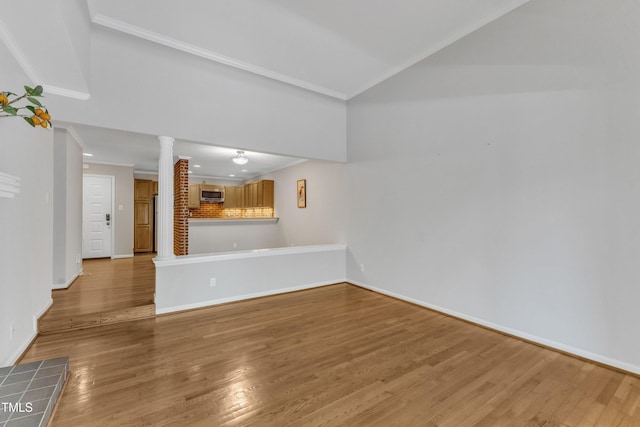 unfurnished living room featuring decorative columns, wood finished floors, ornamental molding, baseboards, and lofted ceiling