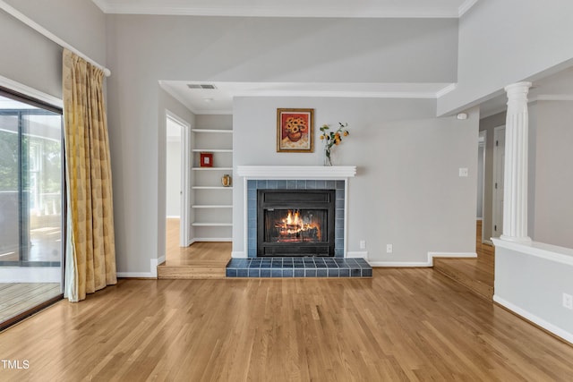 unfurnished living room with a tile fireplace, wood finished floors, crown molding, baseboards, and built in features