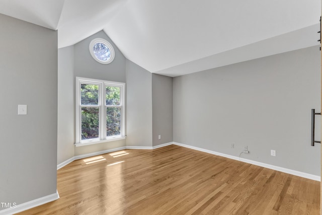 spare room featuring vaulted ceiling, light wood-style flooring, and baseboards