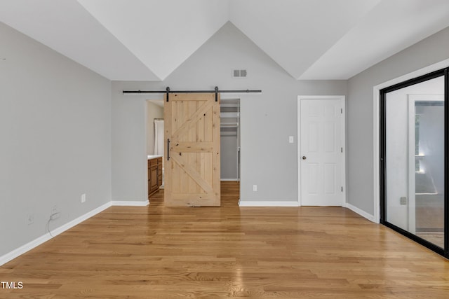 unfurnished bedroom with a barn door, light wood-type flooring, vaulted ceiling, and baseboards