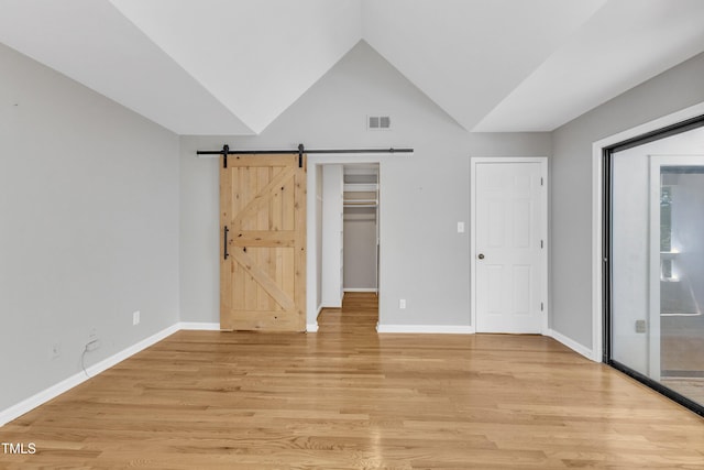 unfurnished bedroom with light wood finished floors, a barn door, lofted ceiling, baseboards, and a walk in closet