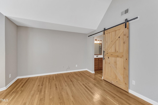 spare room with light wood-style floors, a barn door, baseboards, a sink, and high vaulted ceiling