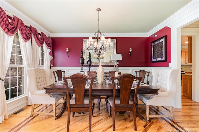  - dining room featuring a chandelier, healthy amount of natural light, wainscoting, a decorative wall, and wood finished floors