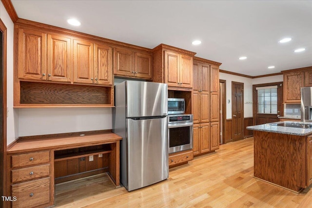 8133 Holly Forest Rd, Wake Forest, NC 27587 - kitchen featuring appliances with stainless steel finishes, crown molding, light wood-style floors, brown cabinetry, and a wainscoted wall
