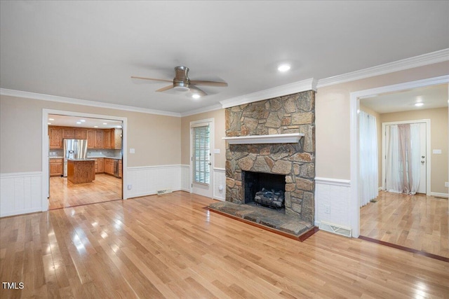 8133 Holly Forest Rd, Wake Forest, NC 27587 - unfurnished living room featuring light wood-style floors, ceiling fan, crown molding, a wainscoted wall, and a fireplace