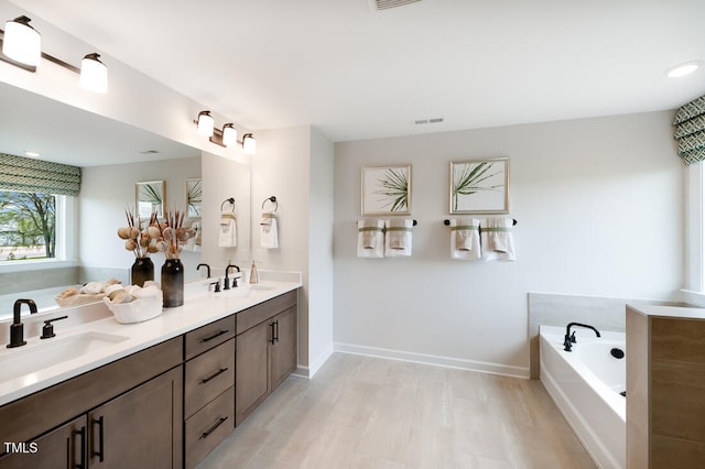 bathroom featuring a garden tub, double vanity, baseboards, and recessed lighting