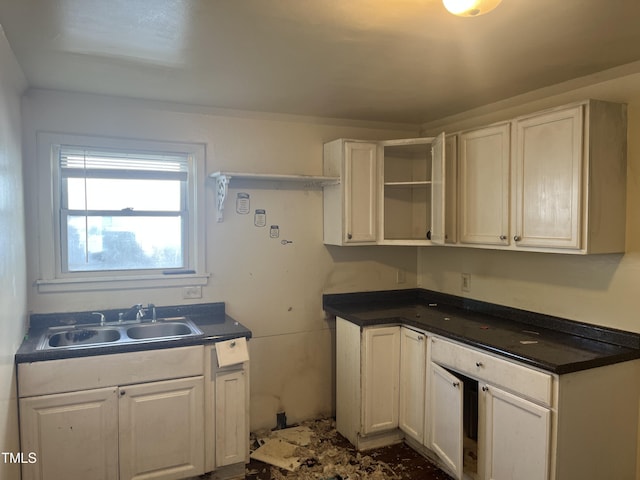 kitchen with a sink, open shelves, dark countertops, and white cabinetry