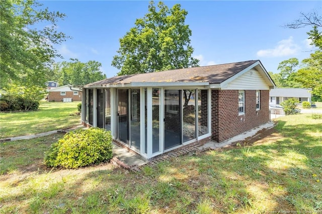 back of house featuring a sunroom, brick siding, and a yard