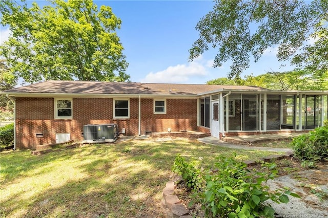 back of house with central AC unit, a sunroom, a lawn, and brick siding