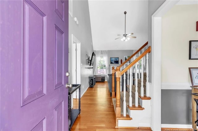 entrance foyer with ceiling fan, stairs, light wood-style floors, and high vaulted ceiling