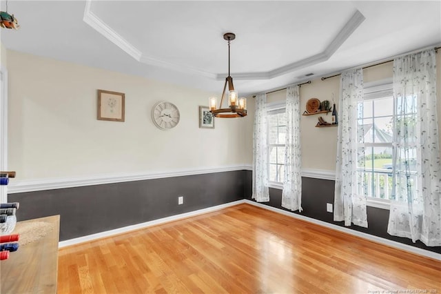 unfurnished dining area featuring a raised ceiling, wood finished floors, a chandelier, crown molding, and baseboards