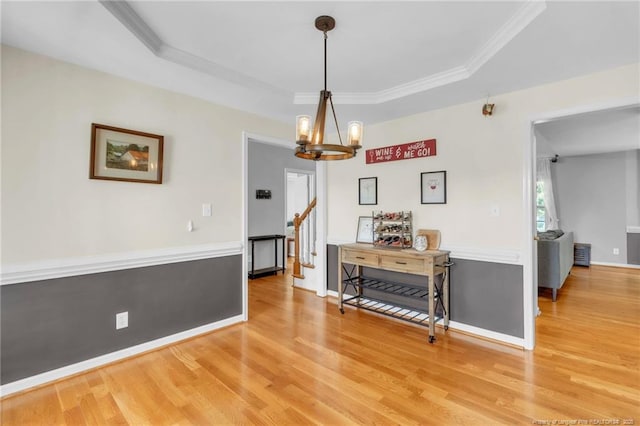 dining room with light wood finished floors, a chandelier, stairs, ornamental molding, and a tray ceiling