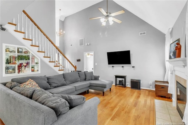 living room featuring ceiling fan, a fireplace with flush hearth, high vaulted ceiling, stairway, and light wood finished floors
