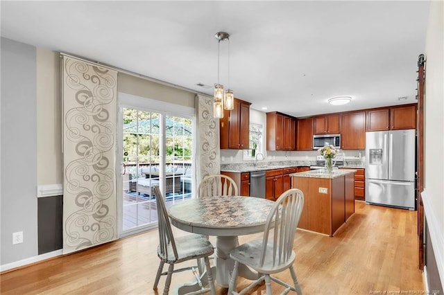 kitchen with appliances with stainless steel finishes, light wood-type flooring, a center island, and a sink