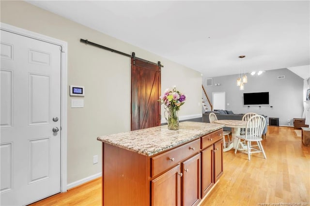 kitchen featuring open floor plan, light wood-type flooring, light stone counters, a kitchen island, and a barn door