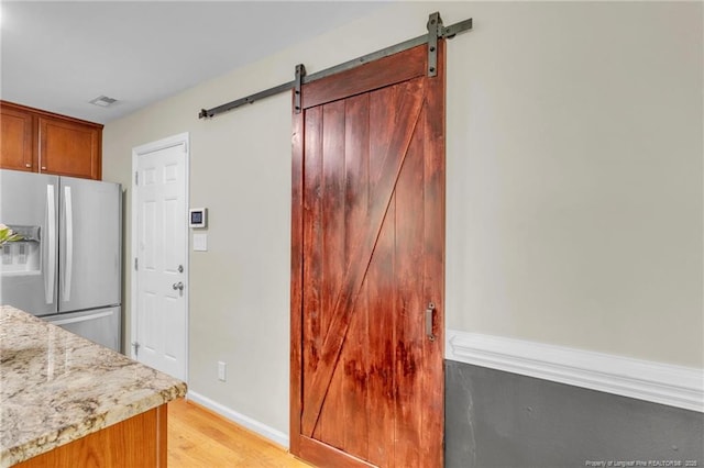 kitchen with stainless steel fridge, a barn door, light wood-style floors, baseboards, and light stone countertops