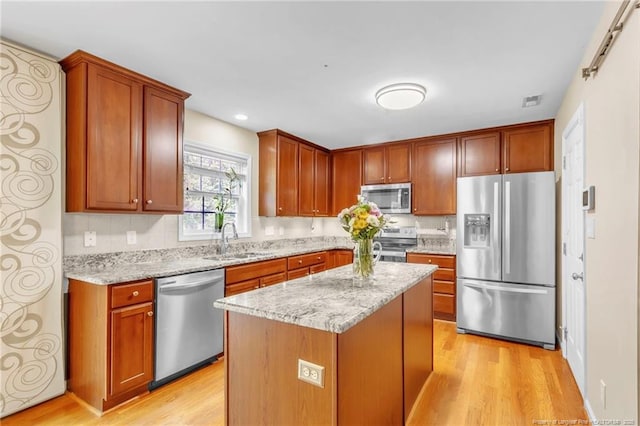 kitchen with stainless steel appliances, a sink, light wood-type flooring, light stone counters, and recessed lighting