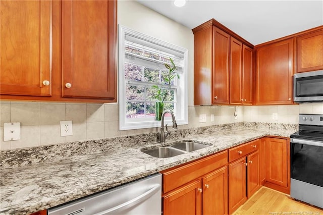 kitchen with appliances with stainless steel finishes, a sink, light stone counters, light wood-style flooring, and backsplash
