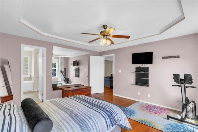 bedroom featuring a tray ceiling, baseboards, wood finished floors, and a ceiling fan