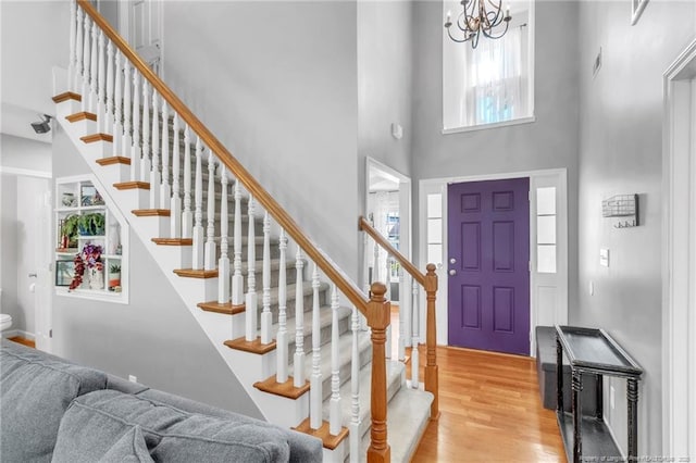 foyer entrance with a towering ceiling, light wood finished floors, stairway, and a chandelier