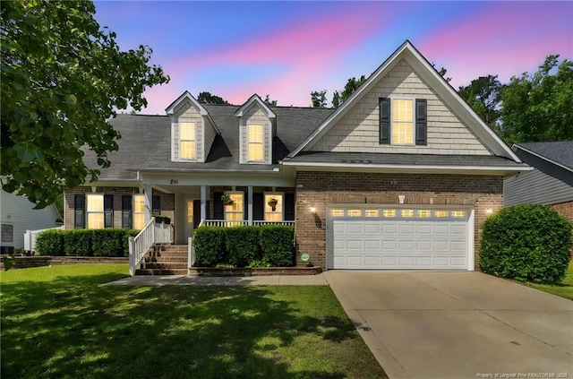 view of front facade with a porch, driveway, a front lawn, brick siding, and an attached garage