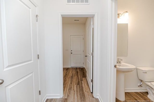 hallway featuring wood finished floors, baseboards, and a sink