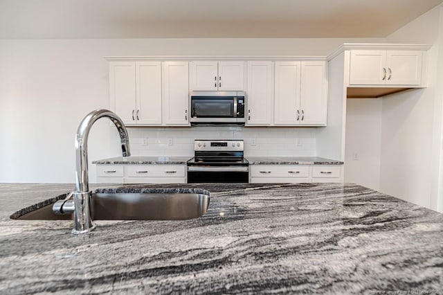 kitchen featuring stainless steel appliances, dark stone counters, a sink, white cabinetry, and decorative backsplash