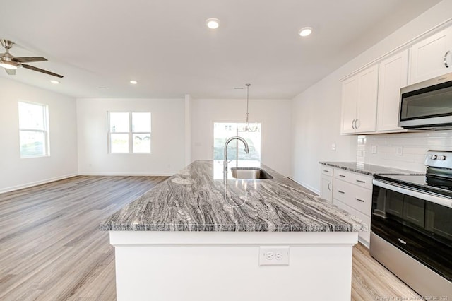 kitchen featuring appliances with stainless steel finishes, a sink, a center island with sink, light wood finished floors, and backsplash