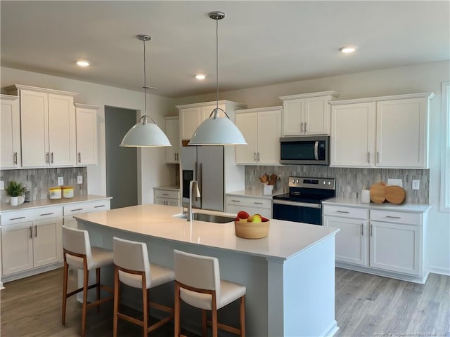 kitchen with stainless steel appliances, a sink, backsplash, an island with sink, and light wood-type flooring