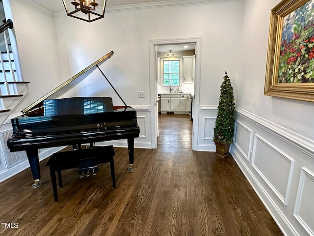 living area featuring a chandelier, ornamental molding, dark wood-style floors, a wainscoted wall, and a decorative wall